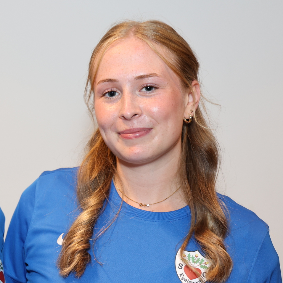 Zwei junge Frauen in blauen Sporttrikots stehen l&auml;chelnd nebeneinander vor einem hellen Hintergrund.