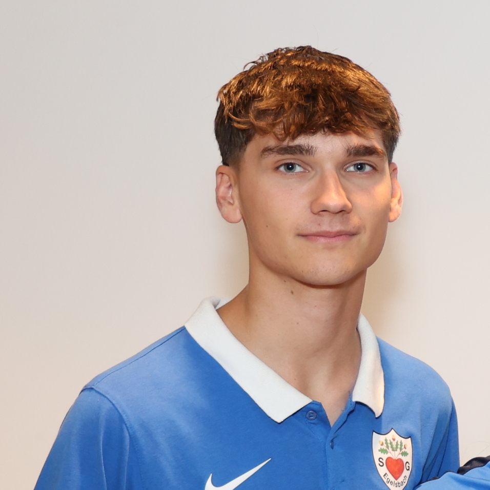 F&uuml;nf Jugendliche in blauen T-Shirts stehen l&auml;chelnd vor einer neutralen Wand.