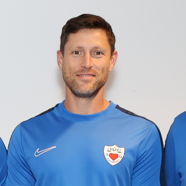 Gruppe von zw&ouml;lf Personen in blauen T-Shirts, die in zwei Reihen auf einem Fliesenboden stehen.