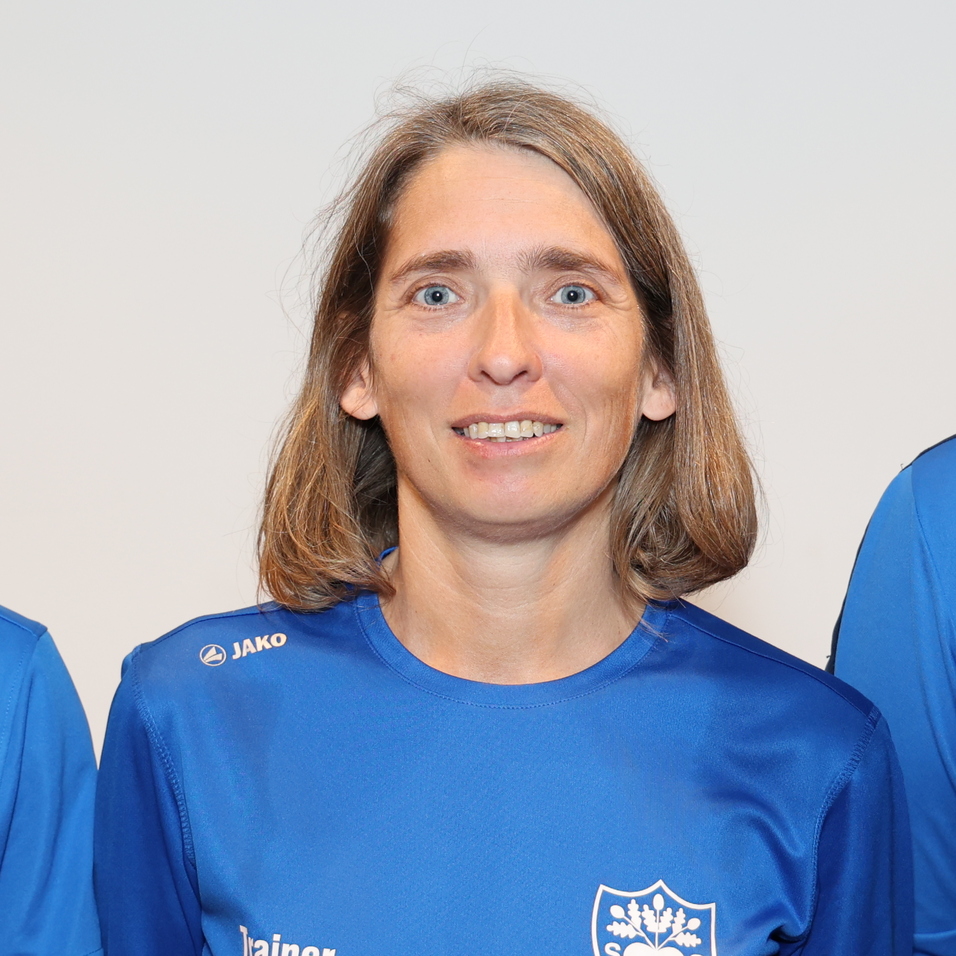 Drei Personen in blauen Sporttrikots stehen vor einem neutralen Hintergrund und l&auml;cheln in die Kamera.