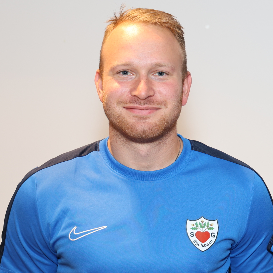 Portr&auml;t von zwei M&auml;nnern in blauen Sporttrikots, l&auml;chelnd, nebeneinander vor neutralem Hintergrund.