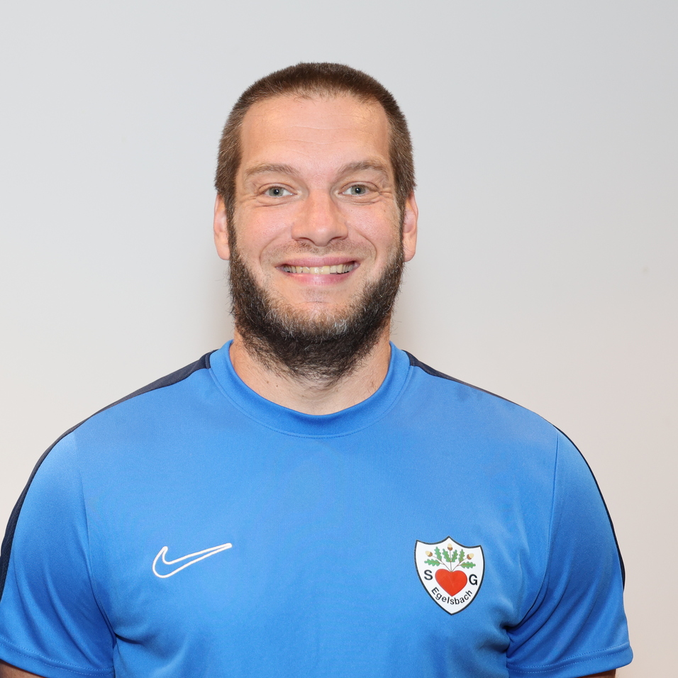 Portr&auml;t von zwei M&auml;nnern in blauen Sporttrikots, l&auml;chelnd, nebeneinander vor neutralem Hintergrund.