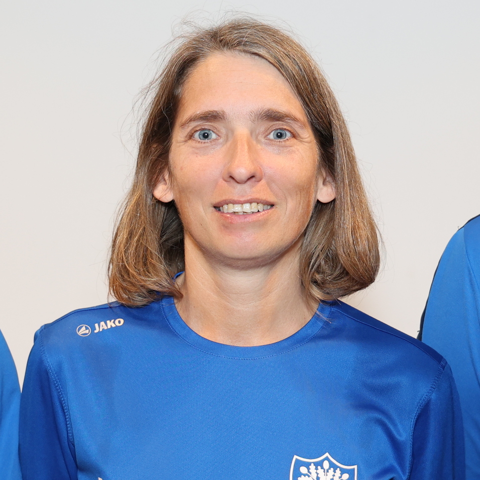 Drei Personen in blauen Sporttrikots stehen vor einem neutralen Hintergrund und l&auml;cheln in die Kamera.