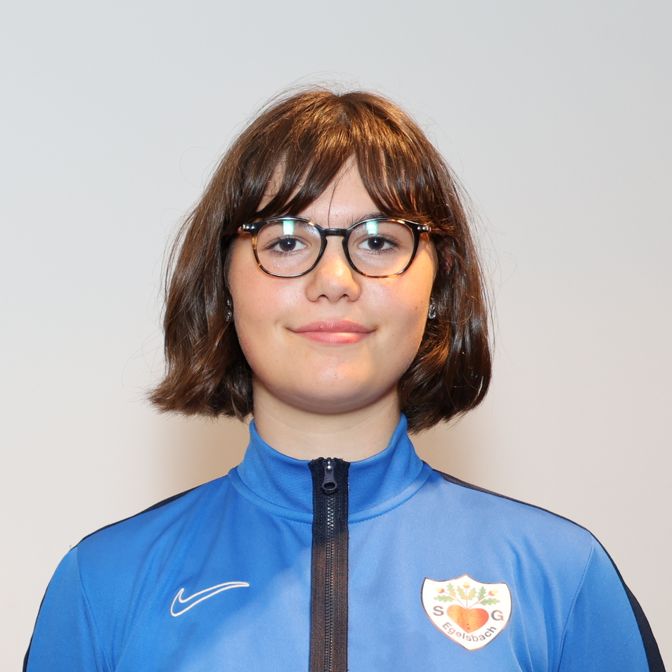 Drei Personen in blauen Sporttrikots stehen vor einem neutralen Hintergrund und l&auml;cheln in die Kamera.