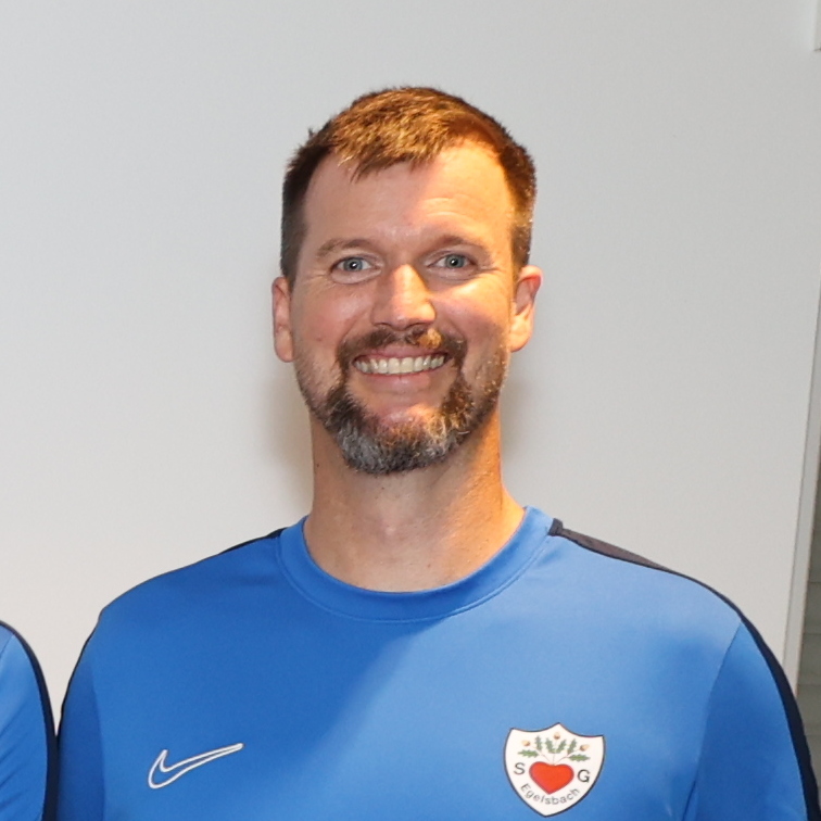 Gruppe von zw&ouml;lf Personen in blauen T-Shirts, die in zwei Reihen auf einem Fliesenboden stehen.