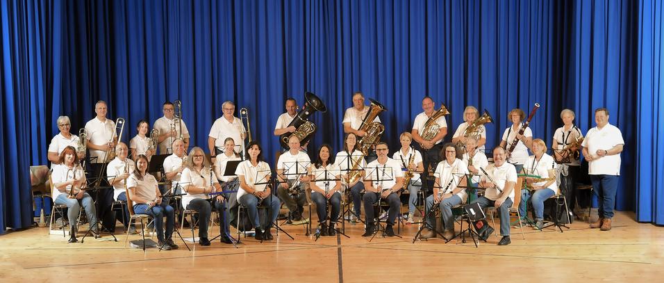 Gruppe von Musikern in wei&szlig;en Hemden posiert auf der B&uuml;hne vor blauer Vorhang, wider verschiedene Instrumente.