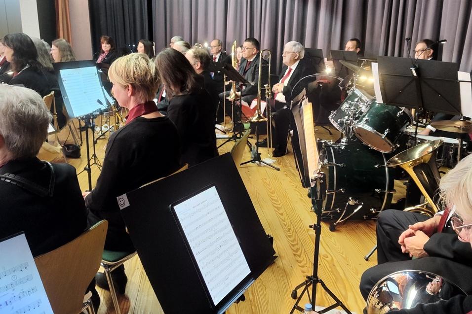 Orchester mit Musikern in schwarzer Kleidung, Instrumente und Notenblätter auf einem Podium während eines Auftritts.