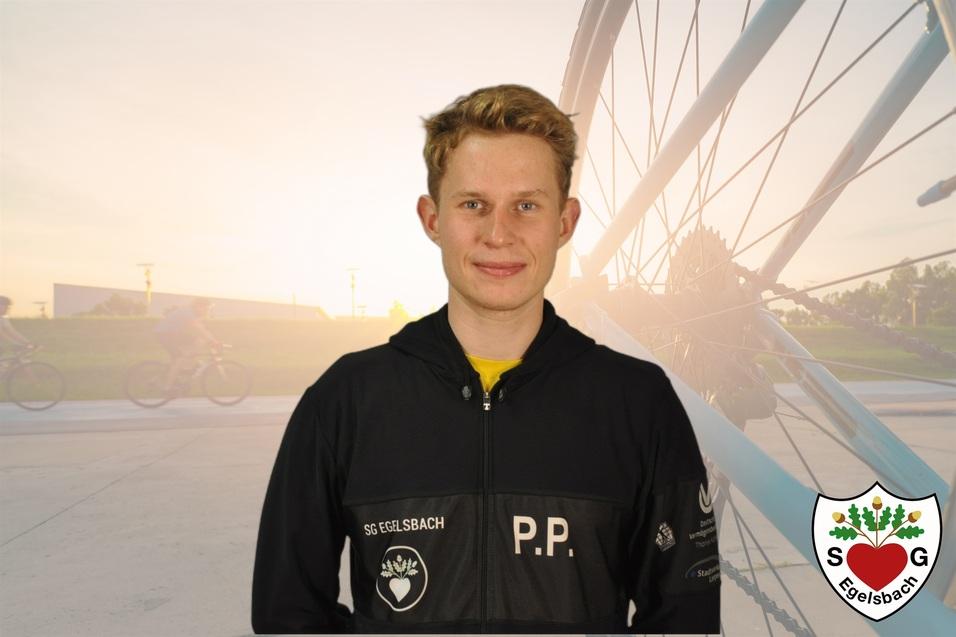 Portr&auml;t eines jungen Mannes in einem dunklen Trainingsanzug, vor verschwommenem Fahrradhintergrund bei Sonnenuntergang.