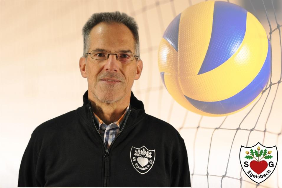 Porträt eines Mannes in einem schwarzen Trainingsjacke vor einem Volleyball und Netz.