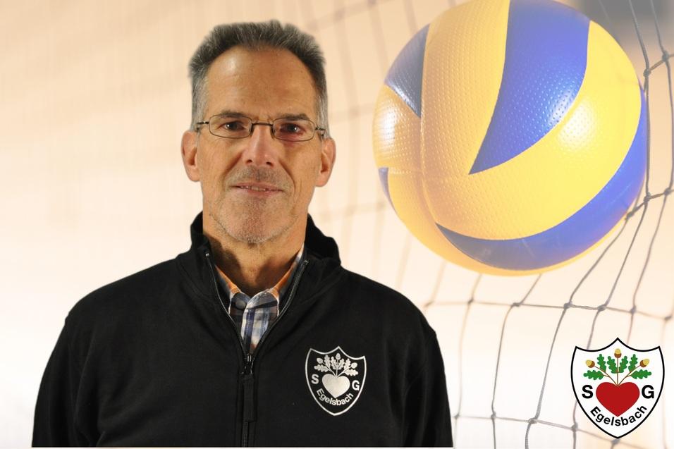 Porträt eines Mannes in einem schwarzen Trainingsjacke vor einem Volleyball und Netz.