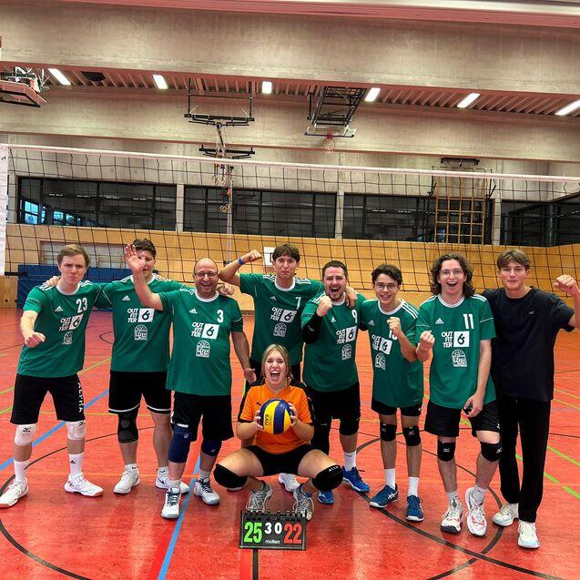 Volleyballmannschaft in gr&uuml;nen Trikots posiert nach dem Spiel in einer Sporthalle, eine Spielerin h&auml;lt den Ball.