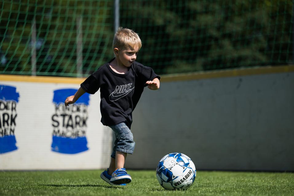 Ein kleiner Junge mit kurzem Haar läuft auf einem Fußballplatz und spielt mit einem Ball.