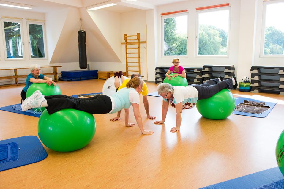 Gruppentraining auf Gymnastikbällen: Frauen führen Übungen in einem hellen Raum mit Holzboden und weißen Wänden aus.